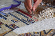 A close up of the hand of a Jordanian mosaic artist making an intricate mosaic using small tiles and tweezers 
