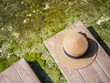 Top view of summer brown hat on wooden footpath and clear water pond or pool for travel, vacation concept
