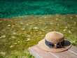 Closeup of summer brown hat on wooden footpath and clear water pond or pool for travel, vacation concept