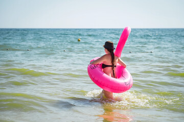 Wall Mural - Pink inflatable flamingo. A girl is swimming in the sea. Sea waves. Cheerful mood. Vacation at the sea.