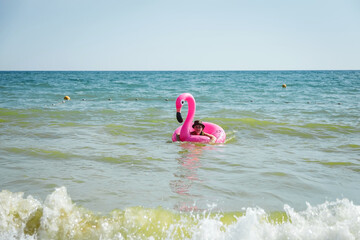 Wall Mural - Pink inflatable flamingo. A girl is swimming in the sea. Sea waves. Cheerful mood. Vacation at the sea.