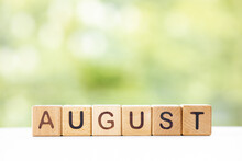 The Word August On Wooden Cubes. They Lie On Other Cubes Against The Backdrop Of The Summer Garden. Month Of Year