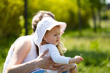 mother holds baby girl with white hat at sunny summer day, outdoor fun