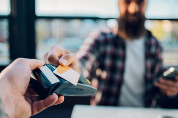 Man making transaction while using credit card and a payment terminal in a cafe