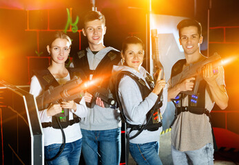 Poster - Happy pleasant cheerful positive young people with laser pistols posing together on dark laser tag labyrinth