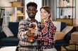 © sofiko14 - Smiling african american man and caucasian woman holding electric screwdriver while standing in embrace at their new house. Concept of family, relocation and happiness.