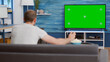 Sports fan watching game on green screen tv mockup encouraging favourite team while relaxing at home sitting on couch. Man sport supporter looking at television with chroma key display in living room.