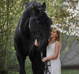 Canvas Print - Beautiful little girl with white hair in a spring wreath in the garden with a friesian horse