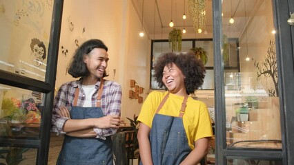 Wall Mural - Two young startup barista partners with aprons stand at casual cafe door, arms crossed, laugh and tease together, happy and cheerful smiles with coffee shop service jobs, small business entrepreneurs.