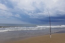 A Surf Fishing Rod On The Beach With A Background Of Dark Sky With Incoming Storm