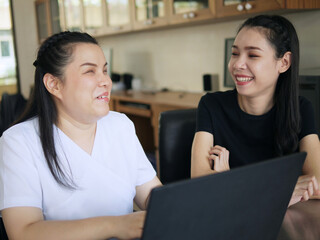 Happy Asian women co-workers in workplace including person with blindness disability using laptop computer with screen reader program for visual impairment people. Disability inclusion at work.