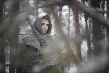 A knight in the armor with the sword in the winter snowy forest.