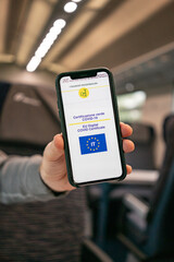 Italian online covid certificate. A man's hand shows a phone screen with a vaccination certificate against the background of the train cabin. High quality photo