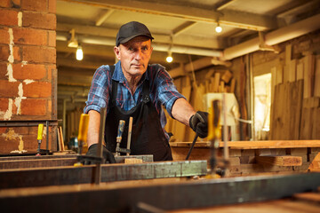 Wall Mural - Portrait of a senior carpenter in uniform gluing wooden bars with hand pressures at the carpentry manufacturing