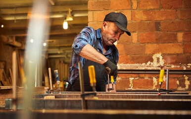 Wall Mural - Portrait of a senior carpenter in uniform gluing wooden bars with hand pressures at the carpentry manufacturing