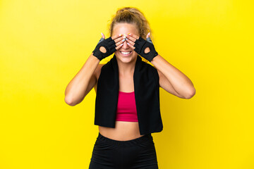 Wall Mural - Sport woman with towel isolated on yellow background covering eyes by hands