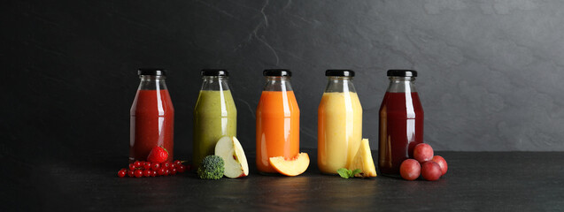 Bottles with delicious colorful juices and fresh ingredients on black table. Banner design