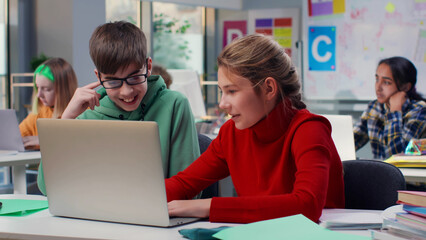 Teenage boy and girl study on laptop together sitting at desk in classroom