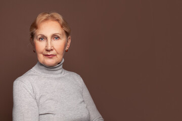 Wall Mural - Mature woman in gray turtleneck on brown banner wall background with copy space