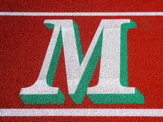 Wall Mural - Two tone white and green letter M painted on running track.