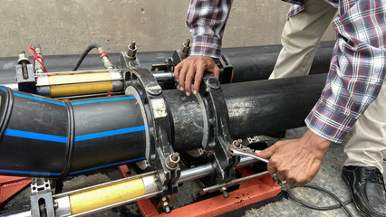 A plumber is working on plumbing with a hydraulic PE pipe welding machine for connecting pipes in a factory.