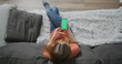 young woman sits down on a sofa and starts using the phone on a green screen. Touching the screen, online internet, browsing. Top view, indoors, medium shot.