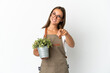 Gardener girl holding a plant over isolated white background pointing front with happy expression