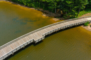 a long winding brown wooden bridge over a rippling silky green lake surrounded by lush green trees a