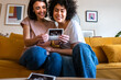 © Daniel - Smiling multiracial lesbian pregnant couple looking baby ultrasounds at home sitting on the couch.