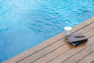 Books and scriptures were placed side by side on wooden terrace by pool and white coffee cup was placed next to Bible. concept of learning the Bible to understand with faith and power of faith in God.