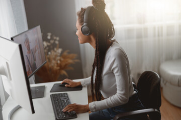 Wall Mural - young happy mixed-race woman speaking on video call on computer wearing headphones