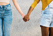 Two multiracial women holding hands - Young adult lesbian couple standing together outdoors