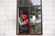 © Ольга Симонова - The window installer adjusts the hinges and checks new windows in the cottage under construction. Ordering windows with golden layout and brown lamination for a private house. A worker in uniform