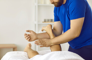 Professional doctor massaging young man's leg. Physiotherapist, massagist, chiropractor or osteopath massaging ankle, shin and calf muscles. Cropped shot. Physiotherapy treatment concept