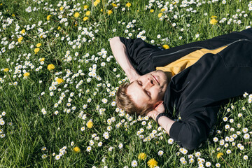 Young man laying in green grass with flowers. People fatigue from work. Summer sleeping and relaxation techniques. Vitamin D sunbathing. Man power nap with eye closed. Rest after work from home