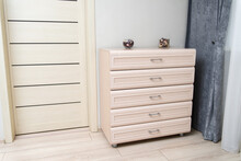 Chest Of Drawers And By The Window With A Gray Curtain In The Room.