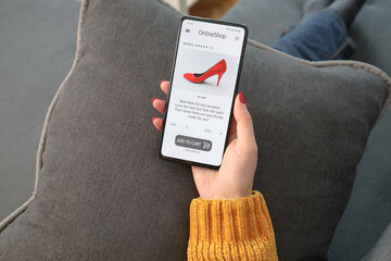 Female hand holding mobile phone with open page of online shoe store on screen. Woman shopping online at home, business and modern lifestyle concept.