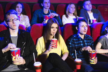 Friends sit and eat popcorn together while watching movies in a movie theater