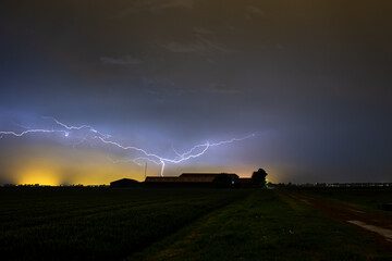 Wall Mural - dramatic image of lightning cleaving the sky above a farm during a thundery night in may. the orange