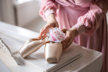 Ballet Pointe Shoes On White Grand Piano. Woman's Hands Put Pink Rose Inside Ballet Shoes.