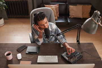 Wall Mural - High angle view portrait of young woman sitting at wooden table in loft home studio adjusting microphone settings using mixing console to start streaming