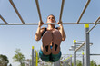 Sporty woman doing a neutral pull-up on the calisthenics bars. Young brunette girl raising her body with her arms holding a fixed bar with her hands for sports.