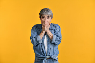 Surprised, happy middle aged Asian woman 50s over colour background. Looking at camera.