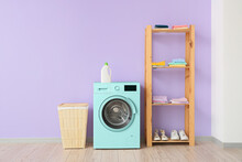 Interior Of Modern Laundry Room With Turquoise Washing Machine, Basket And Shelf Unit Near Lilac Wall