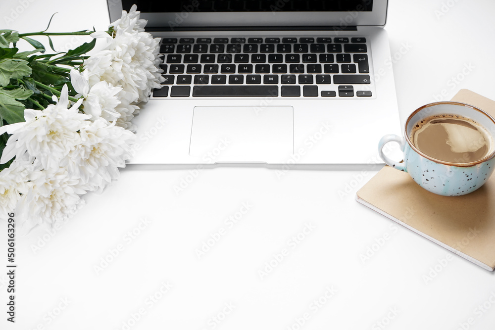 Laptop with flowers and cup of coffee on white background