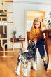 © baranq - Cheerful woman petting her dog while sitting at dinning table at home