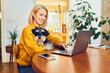 © baranq - Cheerful mature woman using laptop sitting with dog at a table working remotely