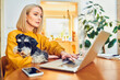 © baranq - Mature woman using laptop holding dog while working from home office