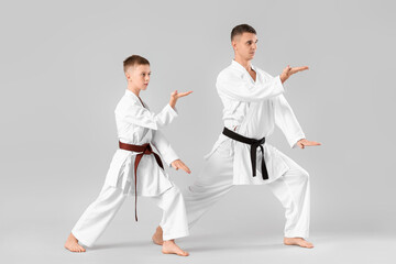 Boy practicing karate with instructor on light background