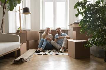 Older 60 couple of new homeowners choosing wall decoration colors, reviewing samples, planning new interior design after relocation, sitting on floor at moving paper boxes